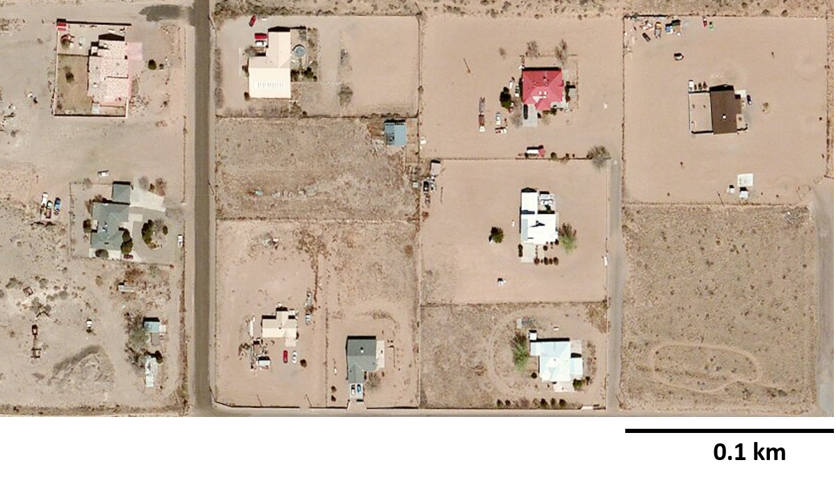 An aerial image of a neighborhood displaying the roofs of houses. A length of 0 point 1 kilometer indicating one fourth of the length of the neighborhood is indicated. There are a total of 9 or 10 houses displayed.